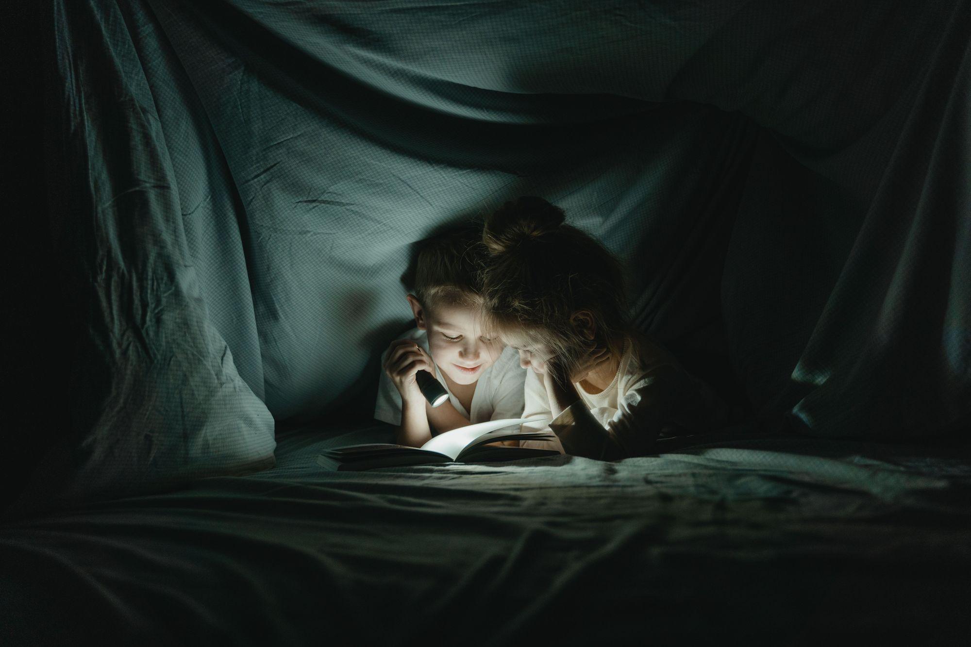 A parent and child reading together inside a cozy blanket fort